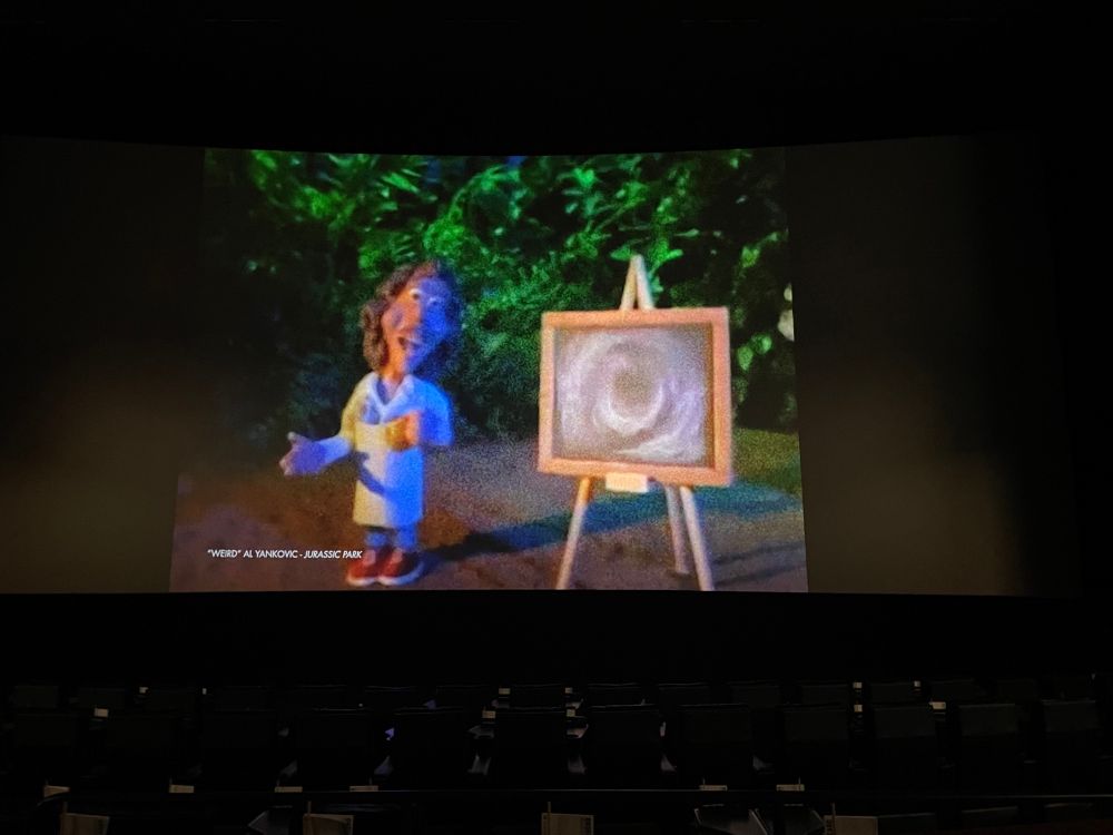 Showing a claymation Weird Al in a Jurassic jungle with a chalkboard showing genetics 
