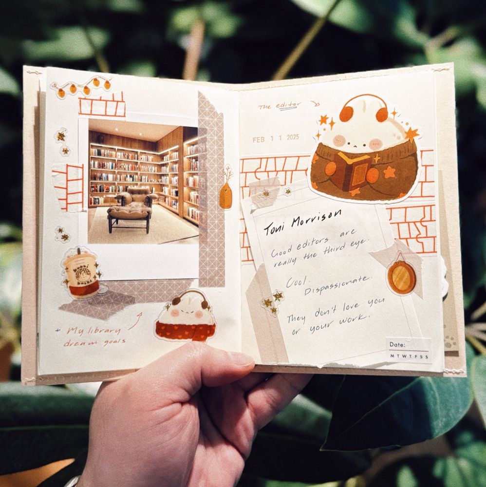 A hand holds open a beautifully designed journal spread with a cozy aesthetic. The left page features a printed photo of a home library with floor-to-ceiling bookshelves and a comfortable reading chair. Around the photo are small decorative stickers and drawings, including a sticker of a bubble tea and a small sticker of a cute bunny. Below the image, handwritten text reads, “My library dream goals.”

The right page contains a handwritten quote from Toni Morrison:
“Good editors are really the third eye. Cool. Dispassionate. They don’t love you or your work.” The quote is written on a piece of paper taped onto the page, surrounded by small star stickers and a mirror drawing. Above the quote, there is a sticker of a cute, round bunny, adding to the cozy and whimsical theme of the spread. The journal background has warm beige and brown tones, accented with red brick patterns and soft geometric designs. The setting includes a blurred background of green leaves, adding a natural and peaceful touch to the scene.
