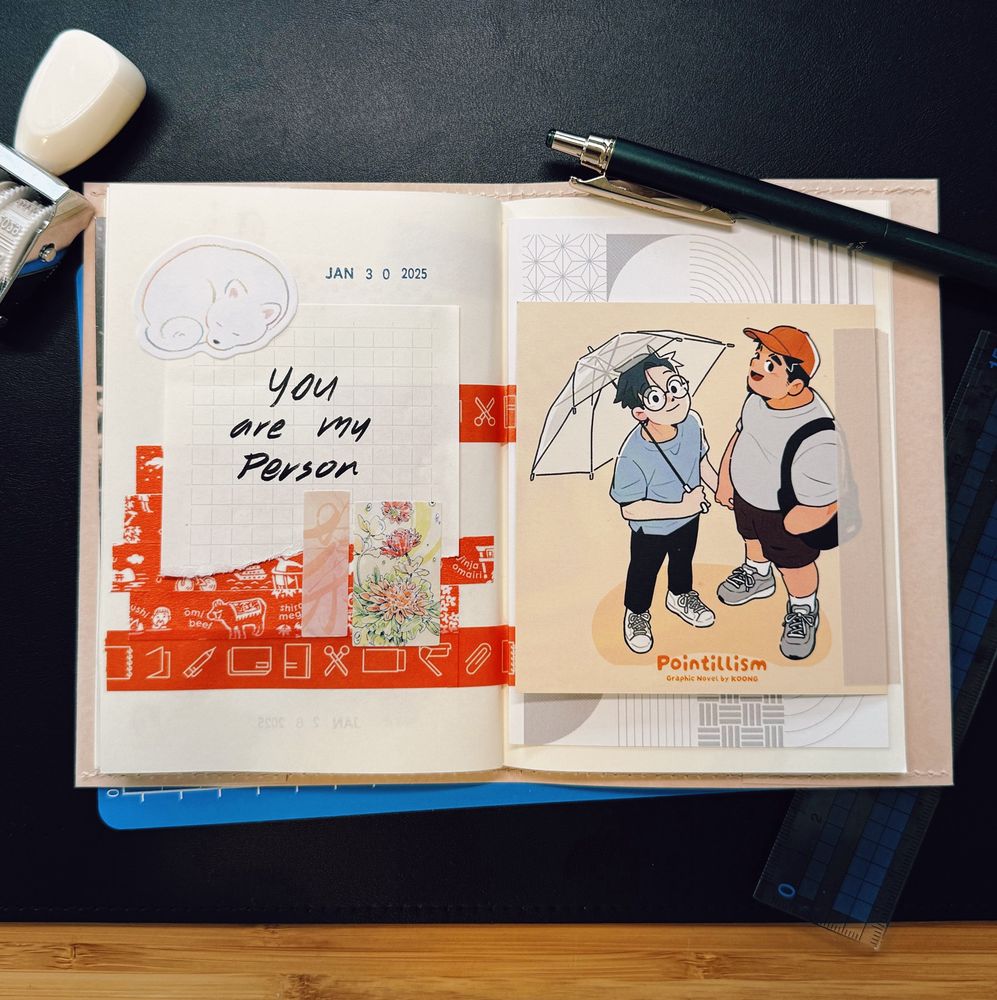 A neatly arranged journal spread on a black desk features an open notebook with creative decorations. On the left page, there is a handwritten message on grid paper that says, “You are my Person,” surrounded by red patterned washi tape, a floral sticker, and a small illustration of a sleeping Shiba Inu. The date “JAN 30 2025” is stamped at the top. On the right page, a postcard-sized illustration from Pointillism, a graphic novel by KOONG, depicts two characters standing together under an umbrella. A dark green pen, a ruler, and a date stamp are placed around the notebook, complementing the workspace setting.