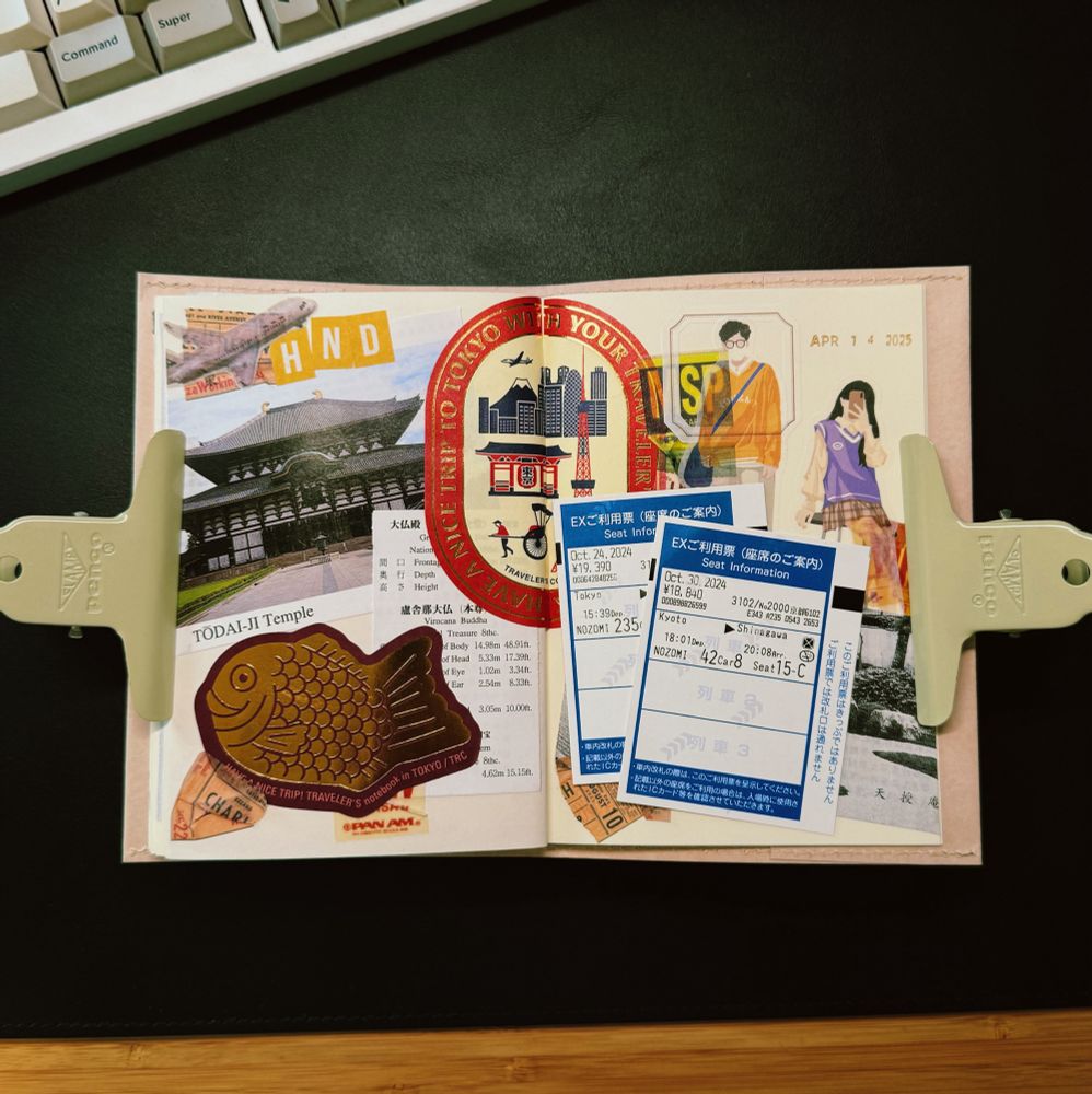 A travel journal spread decorated with tickets, stickers, and photos from a trip to Japan. The left page features a large photo of Todai-ji Temple, a gold taiyaki fish sticker, and various travel-themed stickers including a red circular one that says “Take a trip to Tokyo with your traveler’s notebook.” On the right page, there are two blue and white train tickets (Nozomi Shinkansen from Kyoto to Tokyo), an illustrated couple in fashionable outfits, and the date stamp “APR 14 2025.” The journal is held open with two beige Penco clips on a black desk surface near a mechanical keyboard.