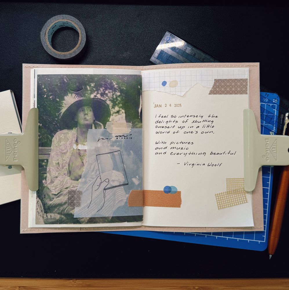 A creative journal spread featuring an aesthetic collage and handwritten text. On the left page, there is an artistic photo of Virginia Woolf in a hat, smoking, overlaid with sketches and transparent elements. On the right page, a quote by Virginia Woolf is handwritten: “I feel so intensely the delights of shutting oneself up in a little world of one’s own, with pictures and music and everything beautiful.” Decorative tapes and papers add texture and visual interest. The journal is held open with clips, and the background includes a cutting mat, ruler, and writing tools.