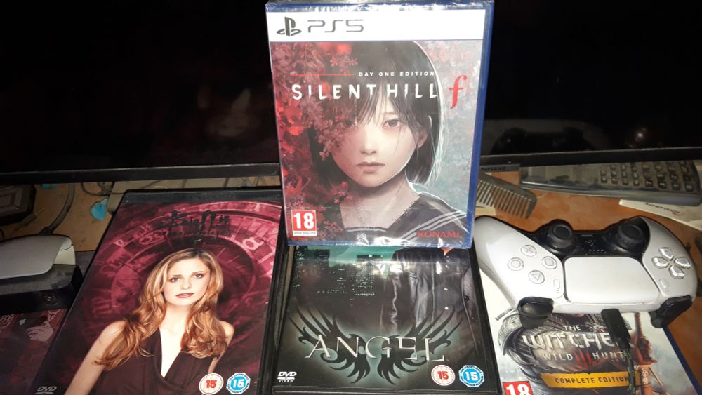 silent hill f for ps5 ontop of buffy and angel dvds with ps5 controller next to them on top of the witcher 3
