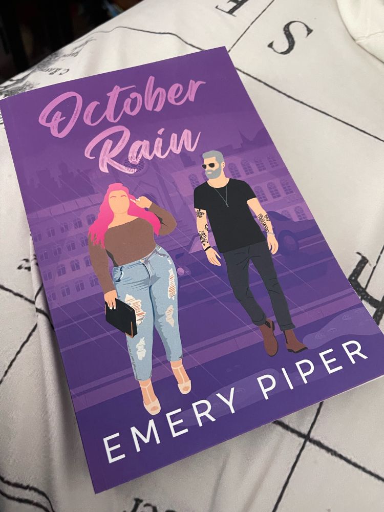 Purple book titled October Rain by Emory Piper. Cover art depicts two of the main characters. One is a light skinned woman with long pink hair. The other is a light skinned man with grey hair and beard.