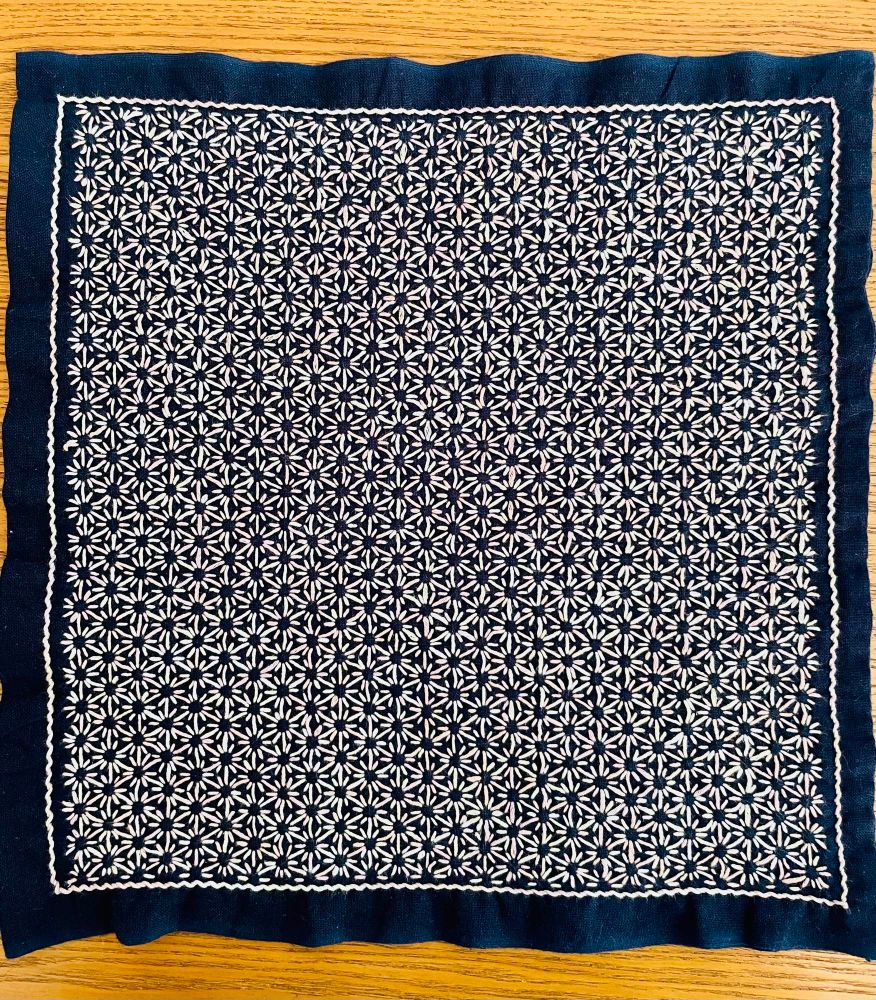 完成した刺し子のふきん、藍色の地に紫から緑系パステルカラーのグラデーション糸で、ひと目麻の葉の刺し子が施してある。