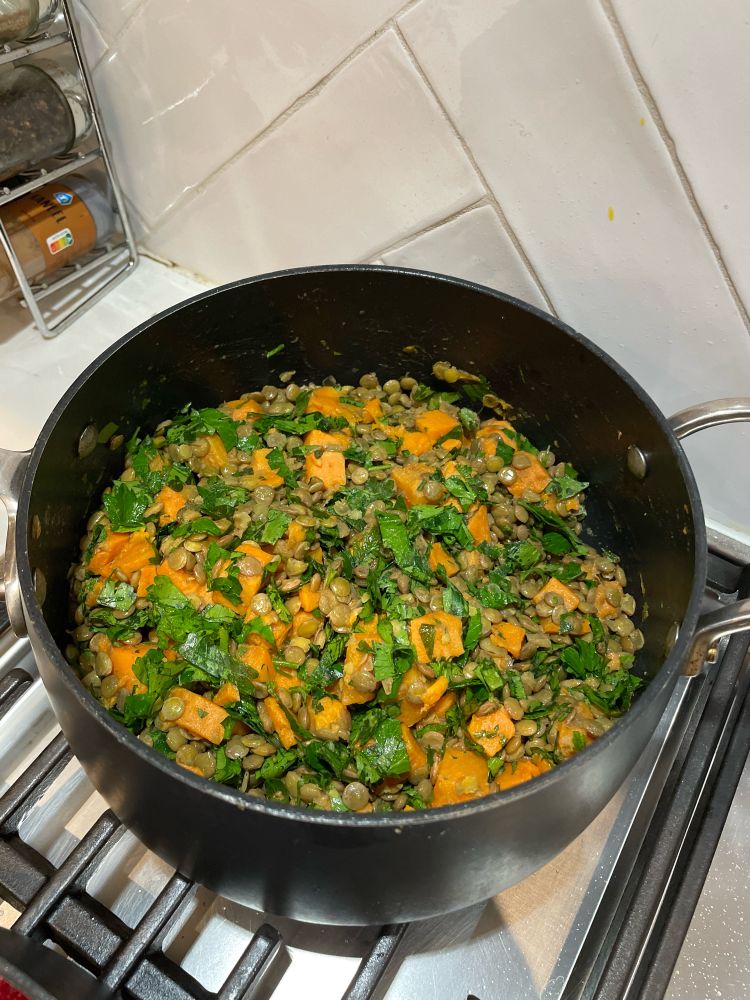 A pot filled with green lentils, sweet potatoes, and parsley. 