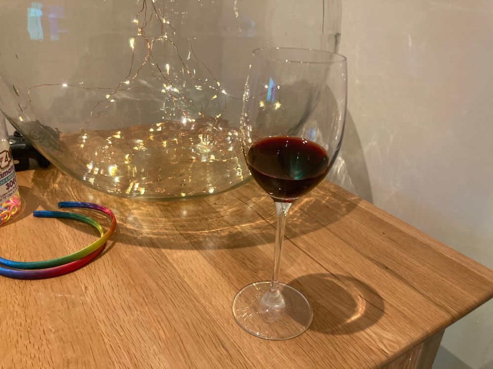 Half a glass of red with on a coffee table, with a jar of fairy lights in the background 
