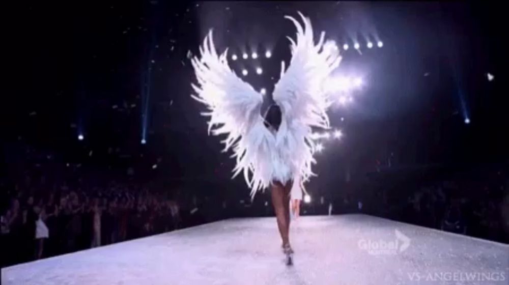 a woman in a white angel costume is walking down a runway in front of a crowd .