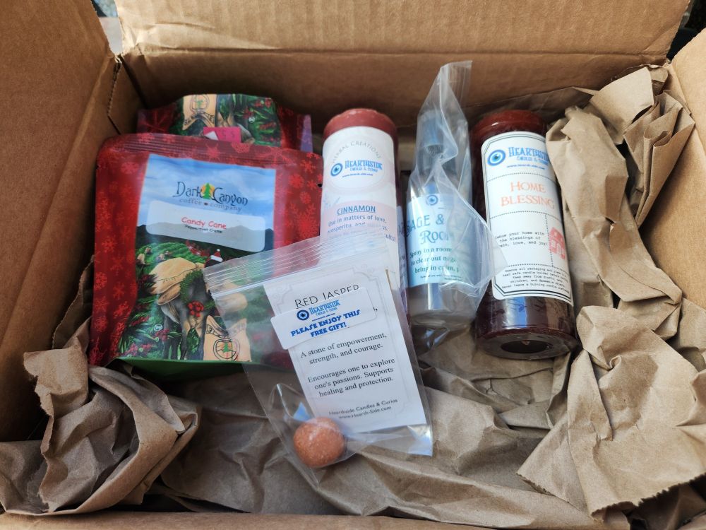 A package with two candles, a room spray, two bags of coffee, and a red jasper stone -- all on top of packing paper.