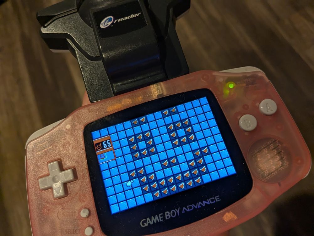 A Game Boy Advance with an E-Reader plugged into it. The game Bomb Hunter is being played and a smily face was drawn into the playing field using flags.