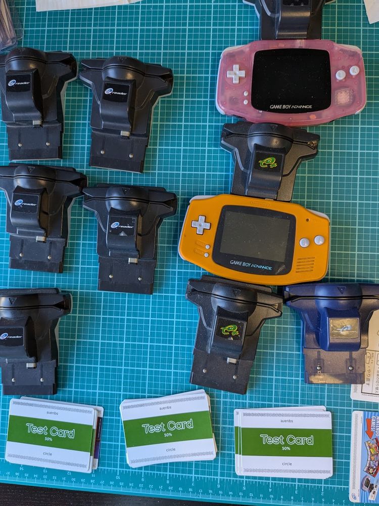  Nine E-Readers, two Game Boy Advances, and three piles of test E-Reader cards, ready to be scanned.
