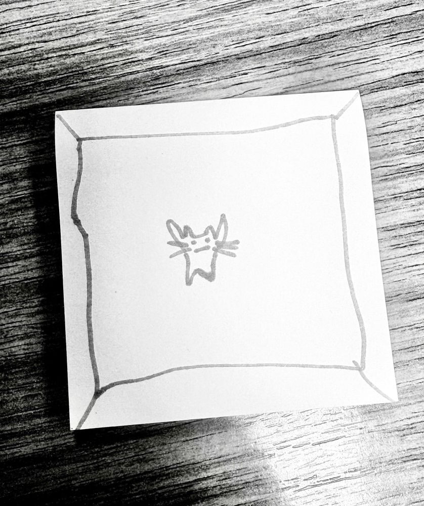 A little cartoon cat drawn on a post it note. It looks like he is in a box

