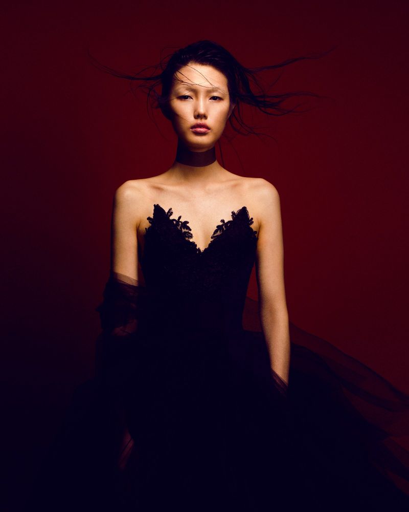 Photograph of model Ma Zizhan by Taylor Horne on red background. Model wears black sculpted "lace"  bodice with exaggerated tulle skirt.