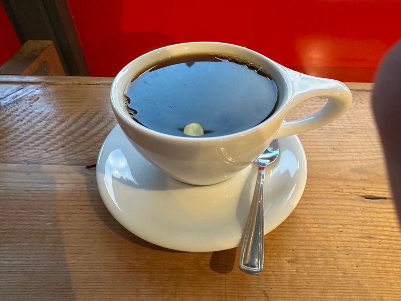 Black coffee in a white cup and saucer on a wooden bar, facing a window onto the street.