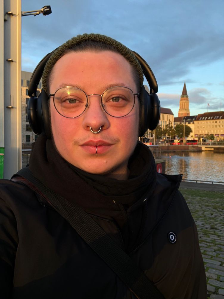 Jay im Licht der aufgehenden Sonne. Mit Mütze und Kopfhörern auf mit der Innenstadt im Hintergrund.