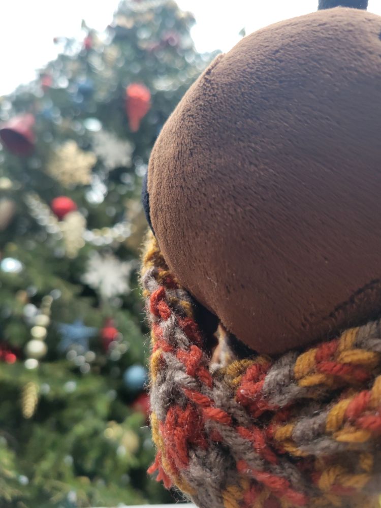 Beenjamin (a plush bee) poses in front of a decorated Christmas tree.