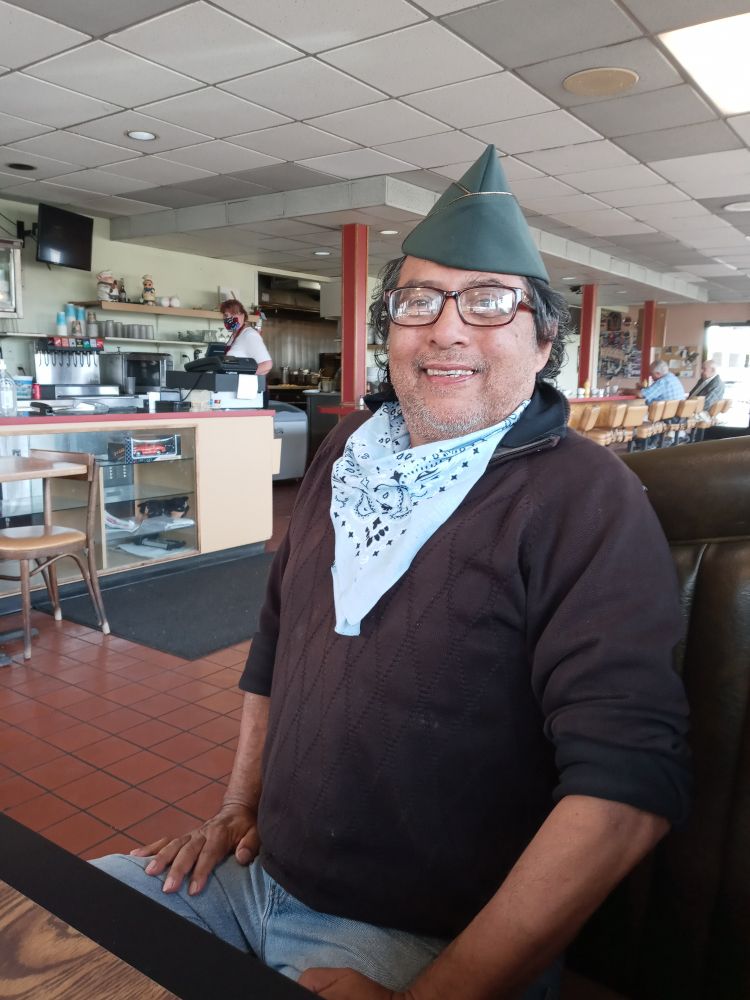 Photo of Richard Talavera in a booth at Dennys wearing an Army dress cap. Maybe Veterans Day? 