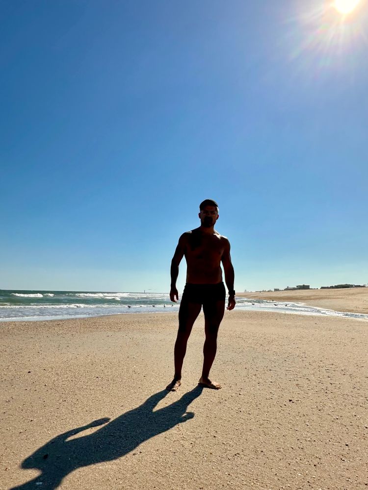Cristian at the beach on a sunny Oct. 6, 2025. Mostly his silhouette and some seagulls far in the background. There are no people around. 