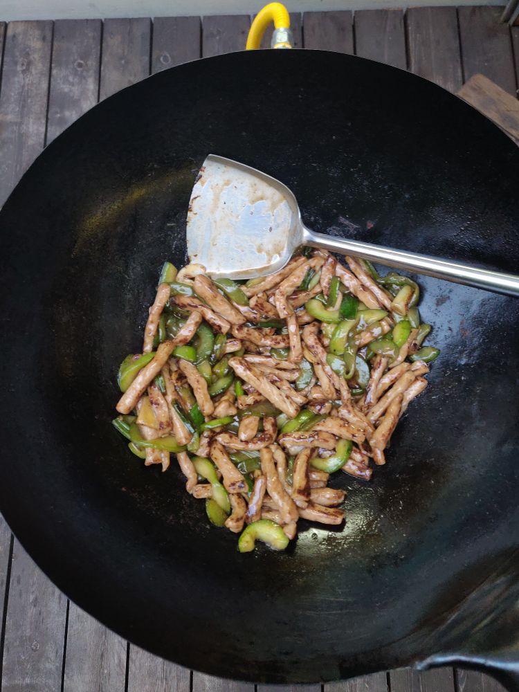 pork loin cut into batons stir-fried with green onion and cucumber in a wok on an outdoor burner