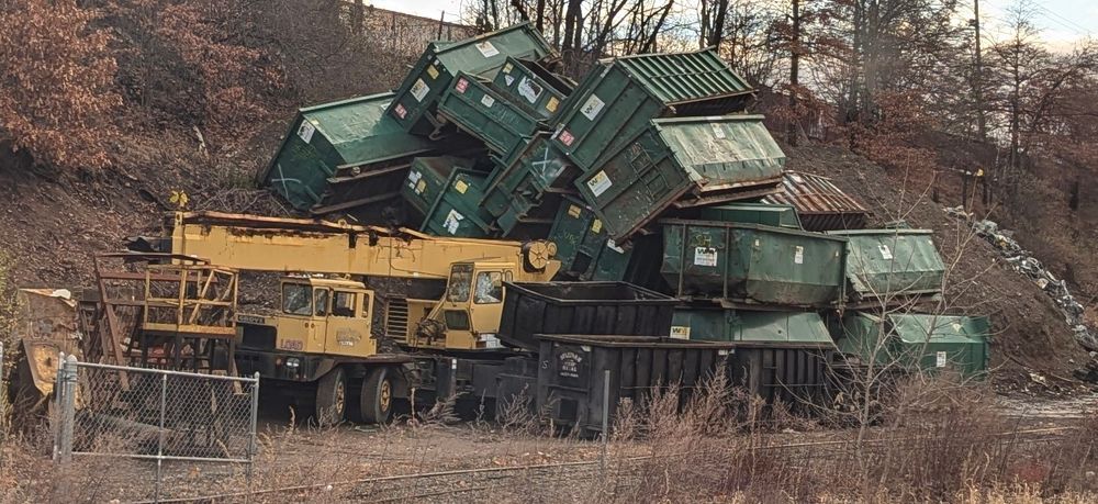 Just an outrageous number (at least 20) of commercial dumpsters piled up against the side of a hill with a giant crane truck sticking out from underneath.