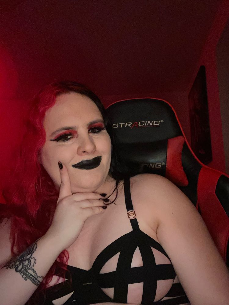 A picture of Persephone at her desk wearing a black cage bra