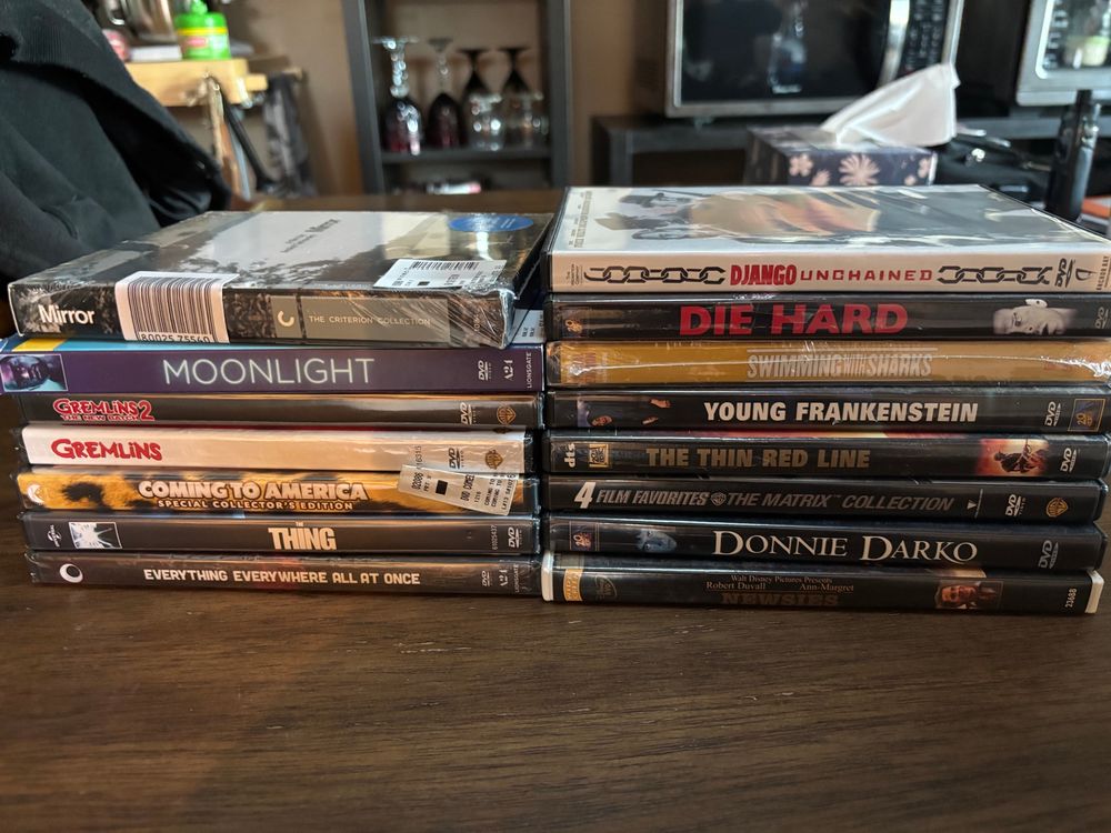A picture of DVDs that were collected this weekend. The films are: 1. Mirror 2. Moonlight 3. Gremlins 4. Gremlins 2 5. Coming to America 6. The Thing 7. Everything Everywhere All at Once 8 Django Unchained 9. Die Hard 10. Swimming with Sharks 11. Young Frankenstein 12. The Thin Red Line 13. Matrix 1-3 + Animatrix 14. Donnie Darko 15. Newsies