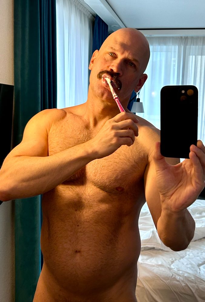 Half naked man in a mirror brushing his teeth