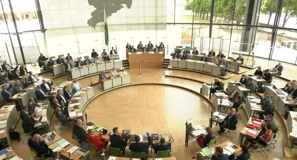 Zu sehen ist das Plenum des sächsischen Landtags während einer offenen Abstimmung. Auf der linken Seite heben die Abgeordneten der AFD den Arm und stimmen somit dem wahlvorschlag zu. Am unteren bildrand ist die CDU-Fraktion zu sehen, die ebenfalls ihre Zustimmung durch gehobenen Arm signalisiert. Oben in der bildmitte ist die sächsische staatsregierung zu sehen, die staatsminister und staatsministerinnen der CDU sowie Ministerpräsident Michael Kretschmer heben ebenfalls ihren Arm. Die Fraktionen von linke SPD und Grüne heben nicht den Arm. 