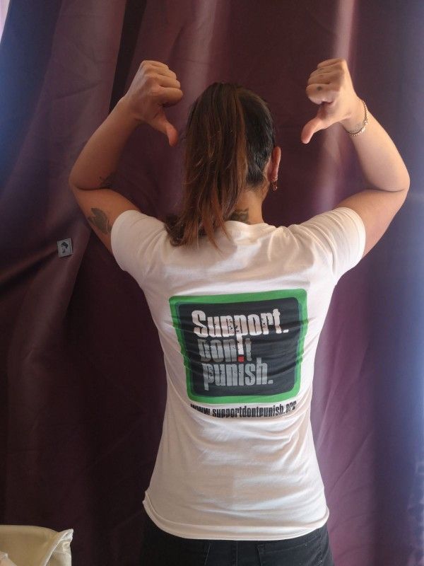 Photo de moi de dos avec un T-shirt blanc portant le logo de la campagne "support. Don't punish."