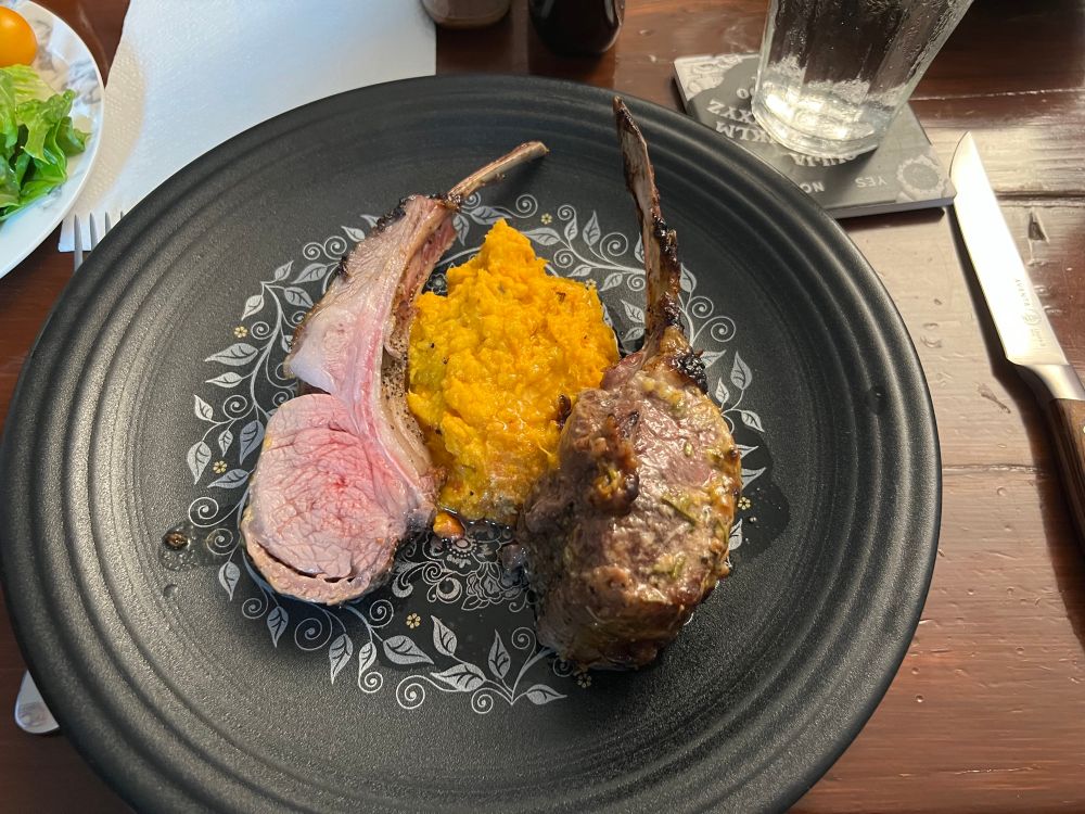 A photograph of two roasted lamb rib chops with a side of mashed sweet potatoes. 