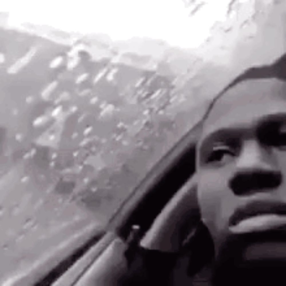 a black and white photo of a man smoking a cigarette while looking out of a car window .