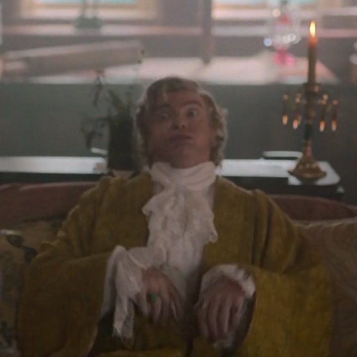 stede from ofmd sitting down onto a couch with a wide-eyed, exaggerated huff