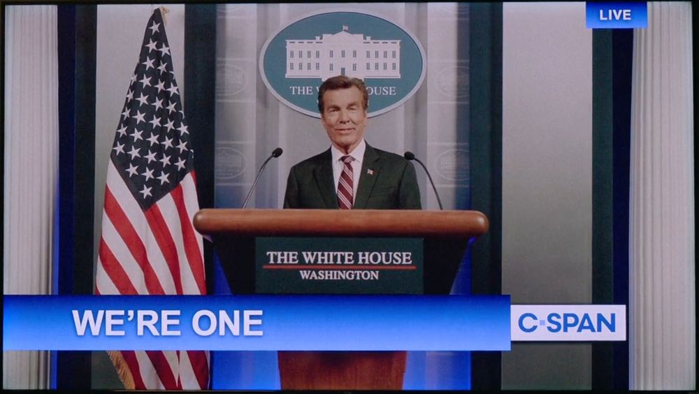 Davis Taffler, a character from the TV show Pluribus, explaining the situation. A chiron below him says "We're One". He is broadcasting on C-SPAN.