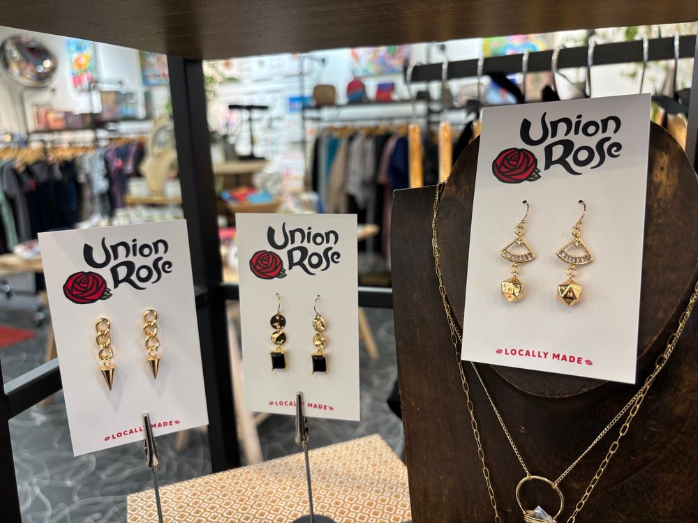 A set of jewelry cards affixed with hanging earrings, arranged in the foreground with the Union Rose shop and racks of hanging clothing visible in the background.