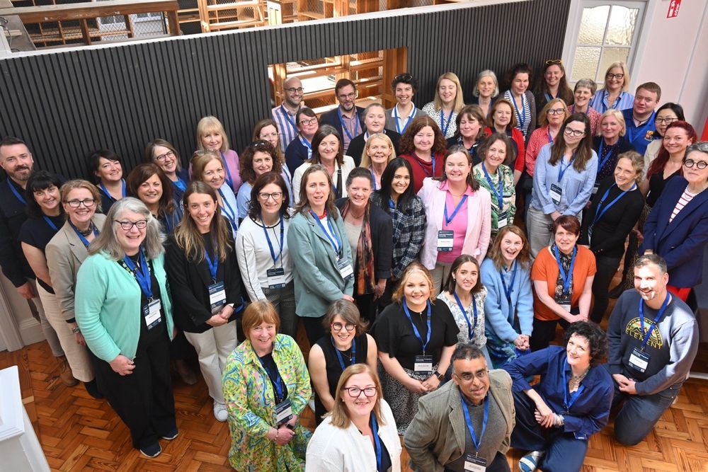 Large group photo of workshop participants standing and smiling at the camera in the Carnegie Library space during the HEA Student-Staff Partnership Workshop, 8 May 2025.
