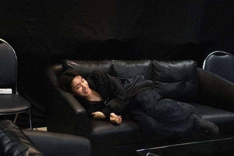 Hobi on a black couch knees bent 