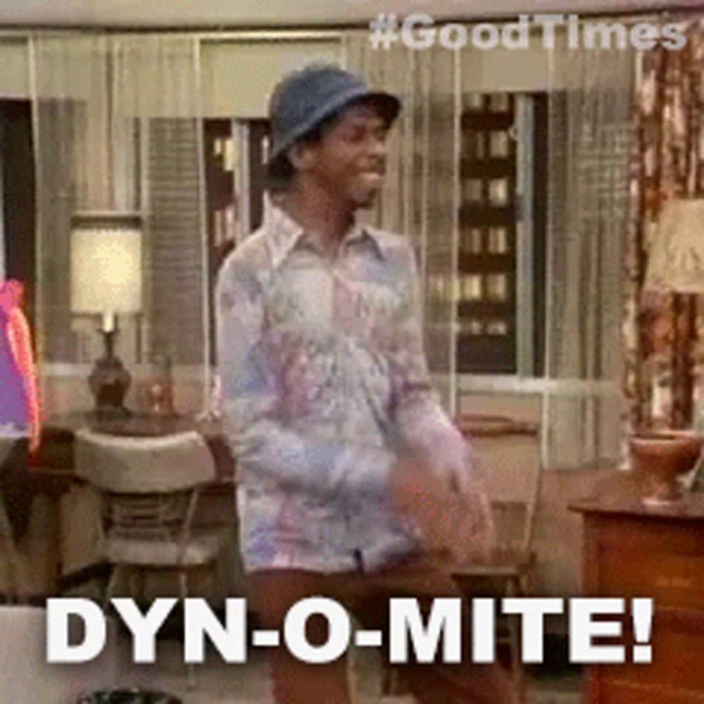 a man in a hat is dancing in a living room with the words dyn-o-mite behind him .