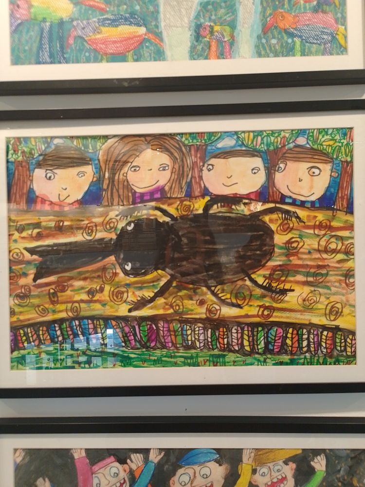 A kid's drawing of a stag beetle on a stick in the foreground, and 4 kids in the background admiring the stag beetle
