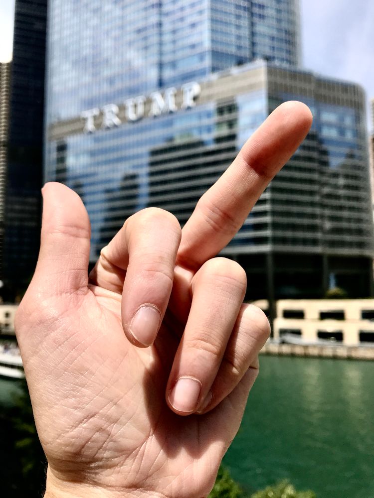 A photo of a white male hand giving the middle finger to Trump Tower in Chicago, Illinois. 