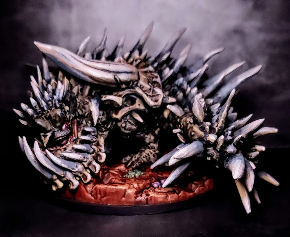 Picture of a hand-painted model of the Monster Hunter World monster Radobaan, a beast absolutely covered in bones & spines, with a glowing eye and face visible on the left side of the screen.