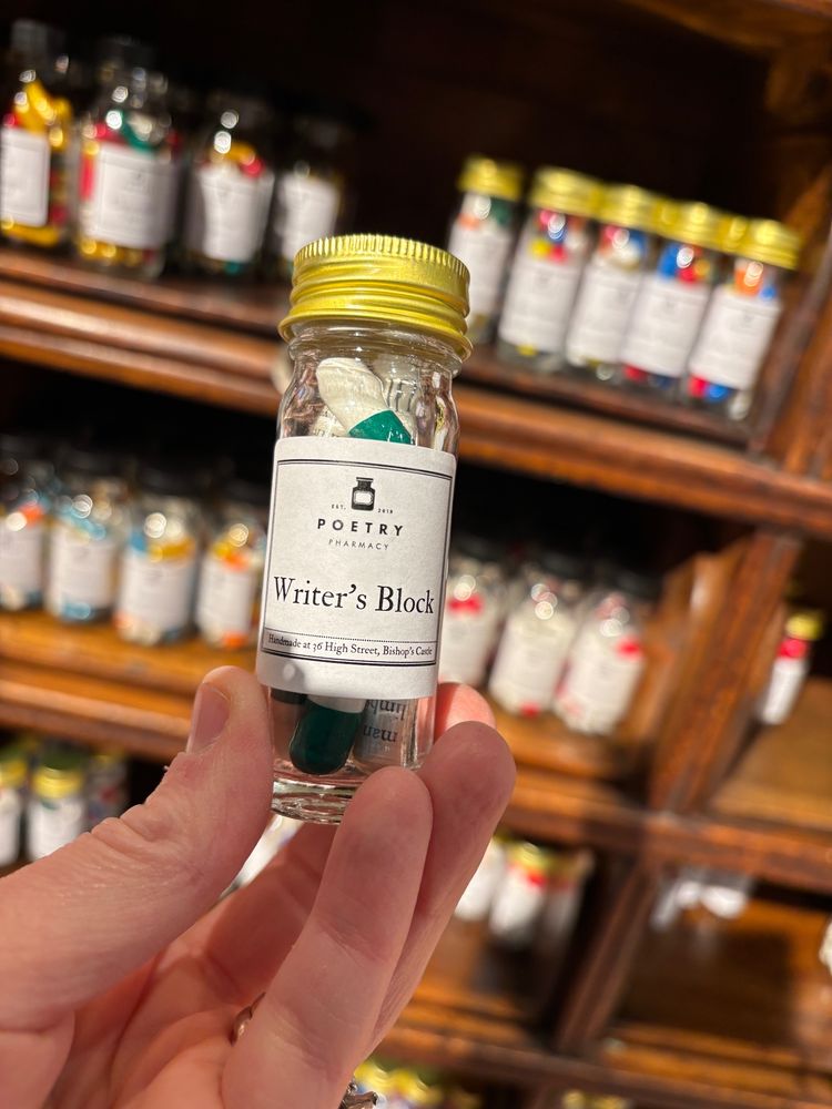 Glass via of pills for writer's block displayed against a shelf with other pills. 