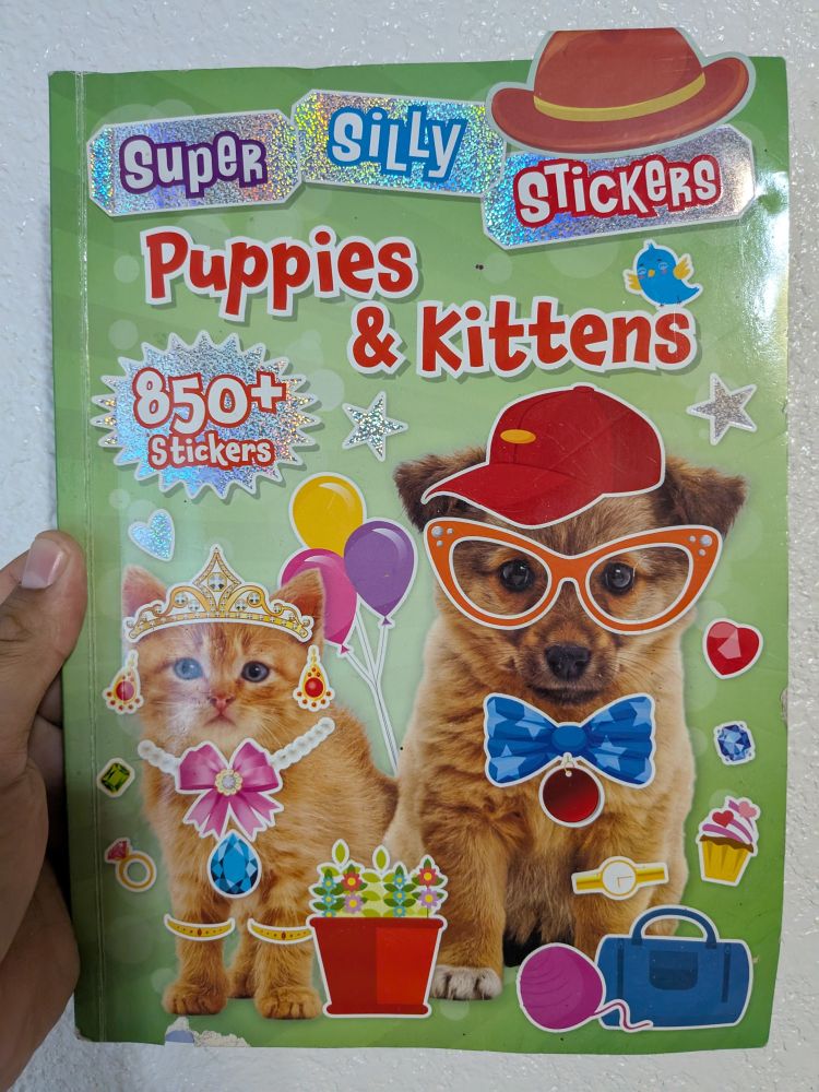 Holding book of kitten and puppy decorated w/ stickers "super Silly stickers Puppies & kitten"