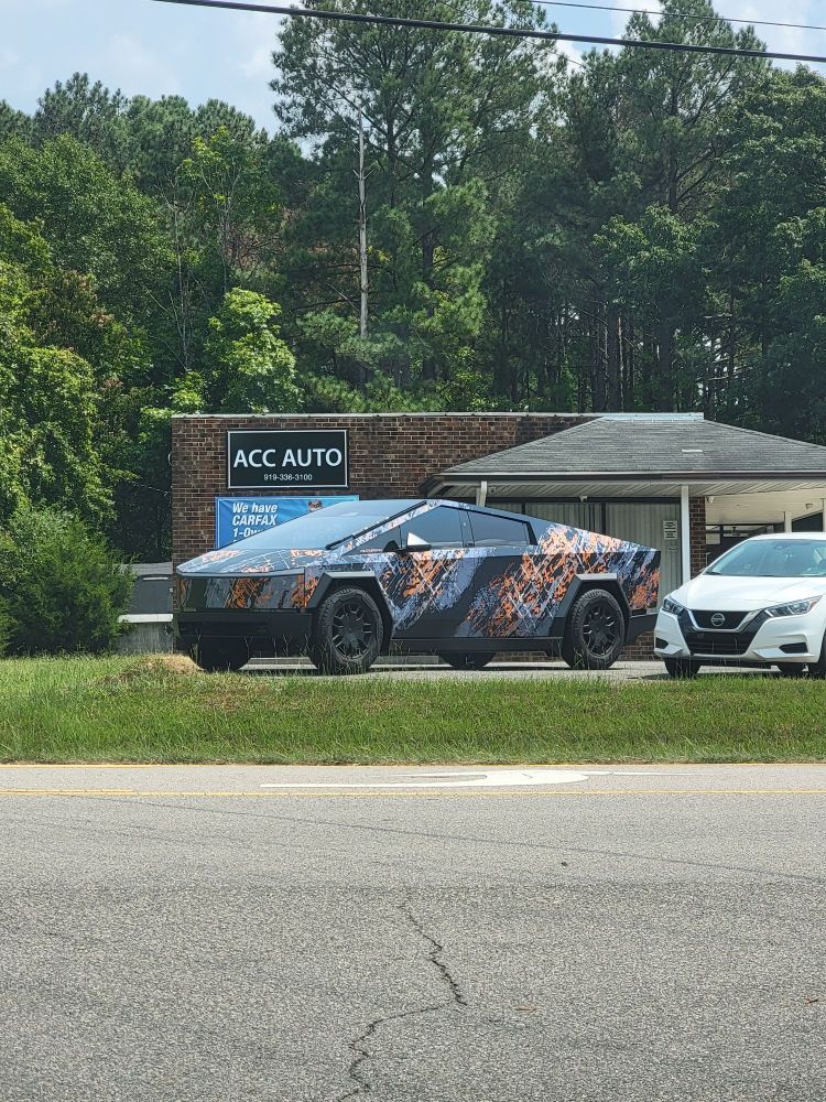 A Tesla cybertruck with a truly garish paint job for sale at a small car dealership.