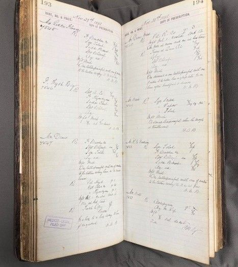 Photograph of a prescription log book, open to show two pages with handwritten text.