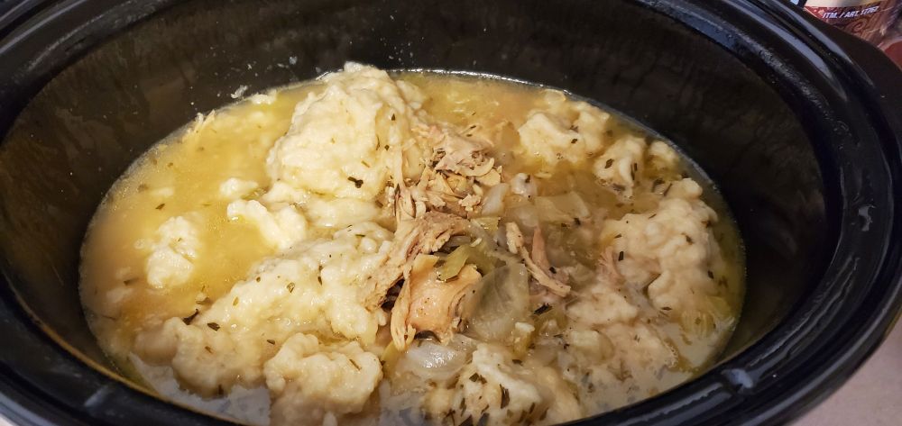 Simmering pot of golden broth, shredded chicken and biscuit dumplings soup sprinkled with flakes of tarragon.