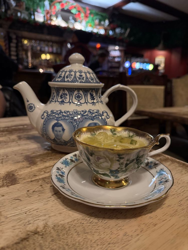 a beautiful teapot and teacup with a faint blue image on it. The teacup is full of a greenish drink and ice. It’s a pot-tail. A cocktail served in a teapot with a tea set. 