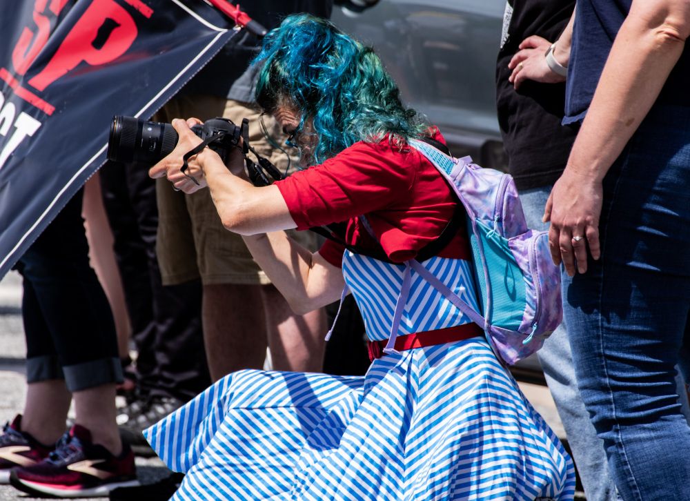 This is a photo of a very colorfully dressed photographer as she's squatting to take a photograph at the "Hands Off" protests from a few weeks back.