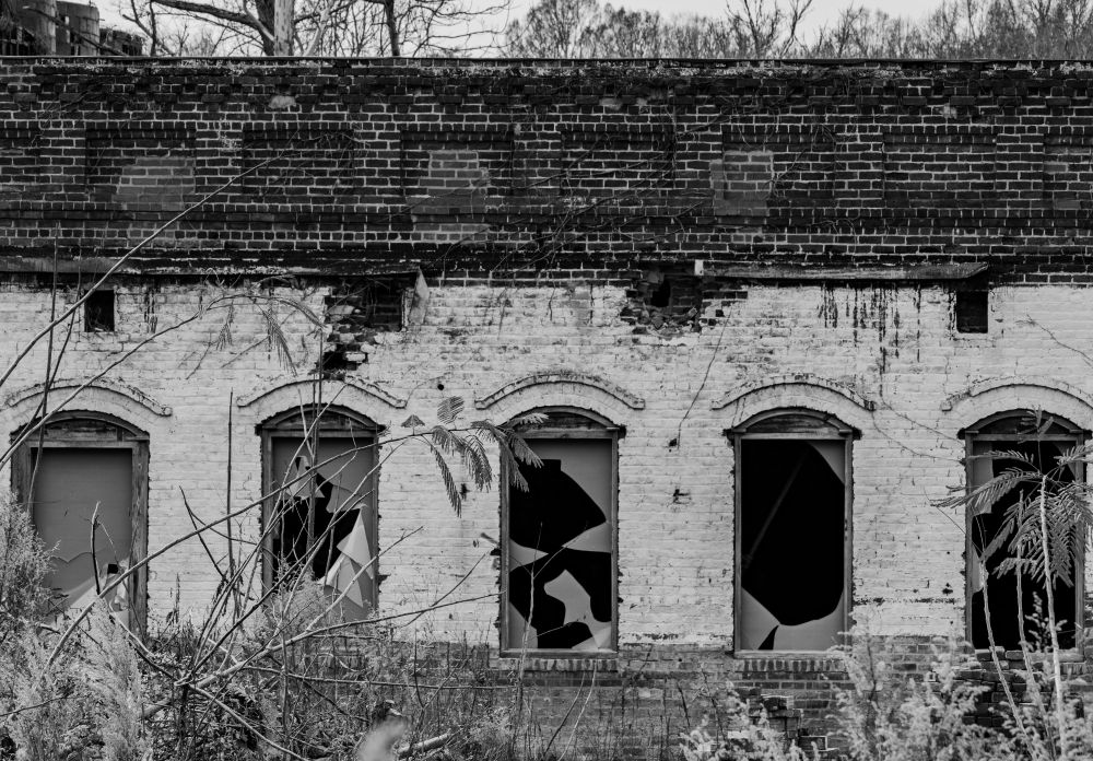 a black and white photo of a section of a building from an old abandoned mill site.  The windows are mostly broken out.