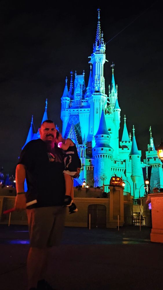 Grimm holding Bean (hiding her face and in a darth Vader dress) infront of the castle at magic kingdom