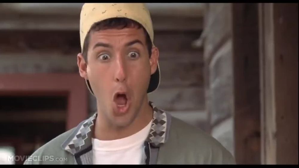 A screenshot of Billy Madison where Adam Sandler is exclaiming, "GOO!". He is wearing a backwards yellow hat and a jacket with diamonds on the collar and a white undershirt. His eyes and mouth are wide open.