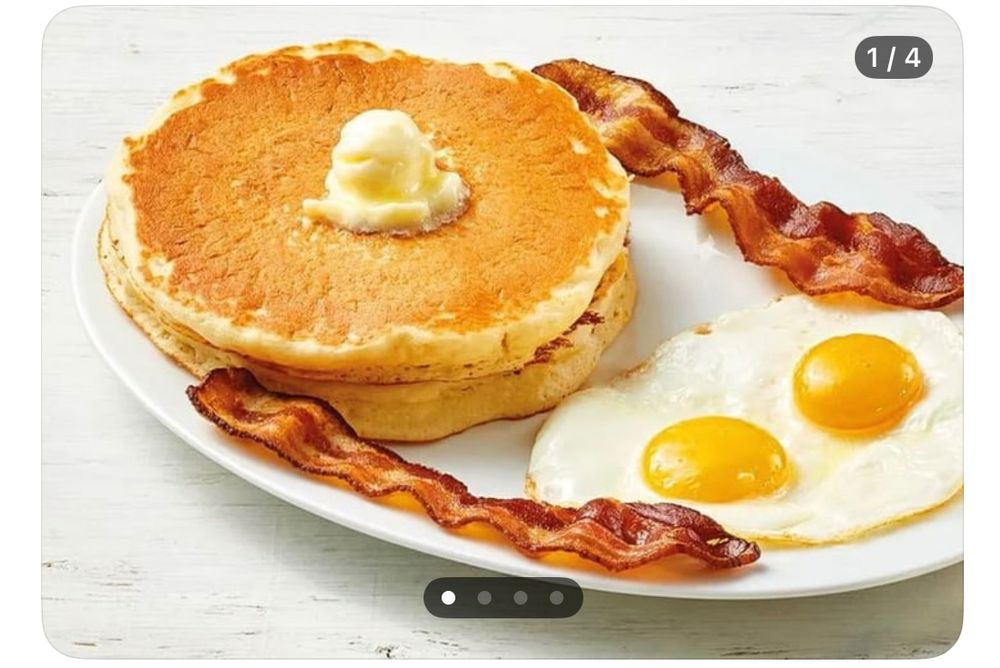 Picture of pancakes with two pieces of bacon connecting to eggs.